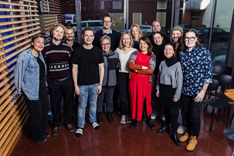 Bild av skådespelarna som ska spela pjäsen Tillsammans hösten 2026 på Wasa Teater. De står framför en glasvgg och tittar glatt in i kameran. Det är 14 personer på bilden varav 12 är skådespelare. De två övriga är teaterchef Linda Zilliacus och regissör Jarno Kuosa